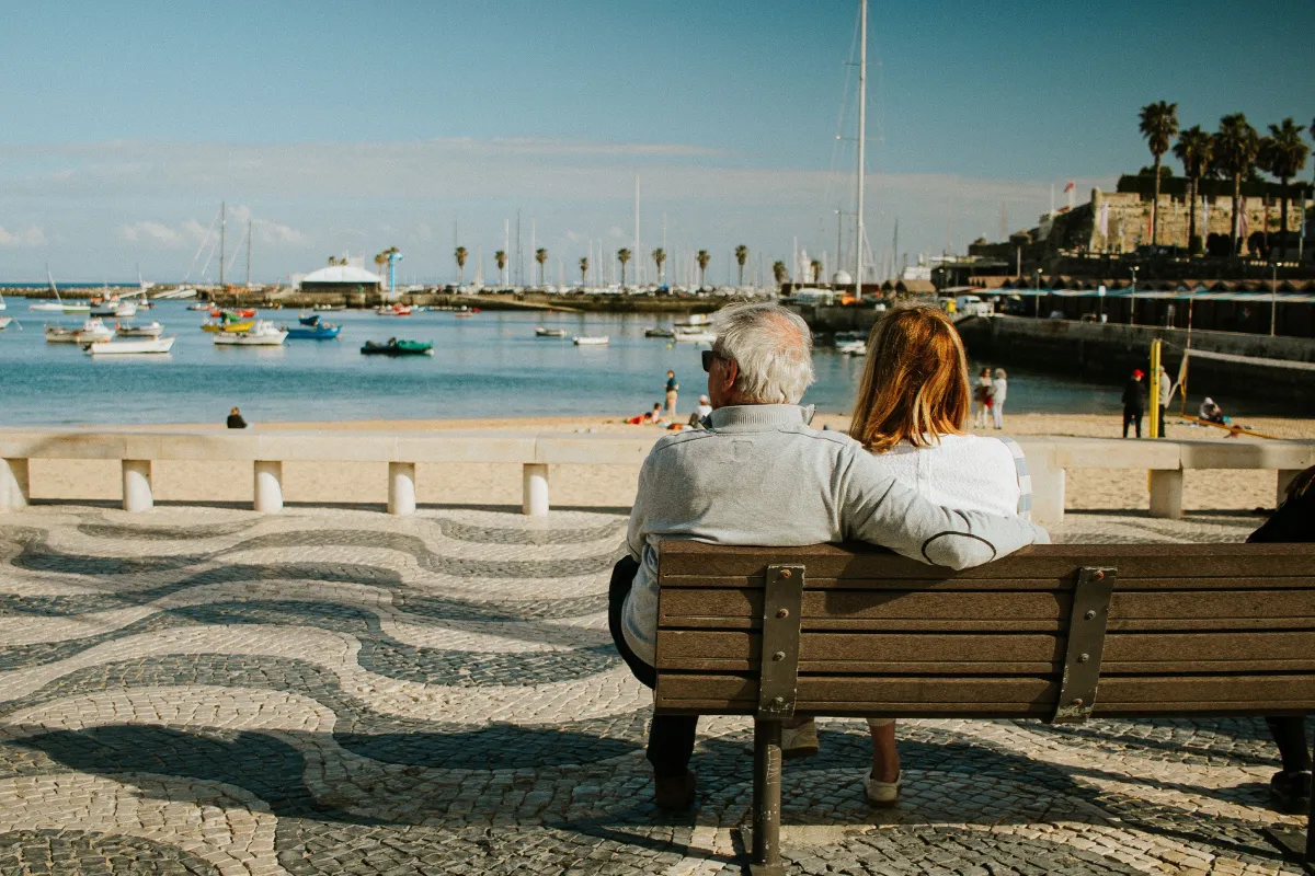 When one spouse retires first: planning for couples with an age gap - An elderly couple relaxing on a bench, overlooking the coast